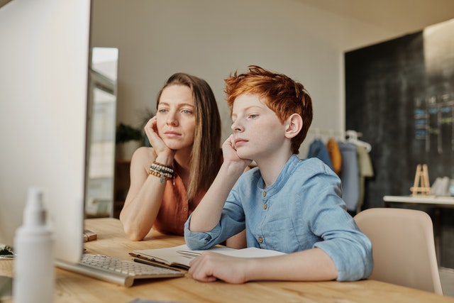 woman and red haired boy at desk looking at computer